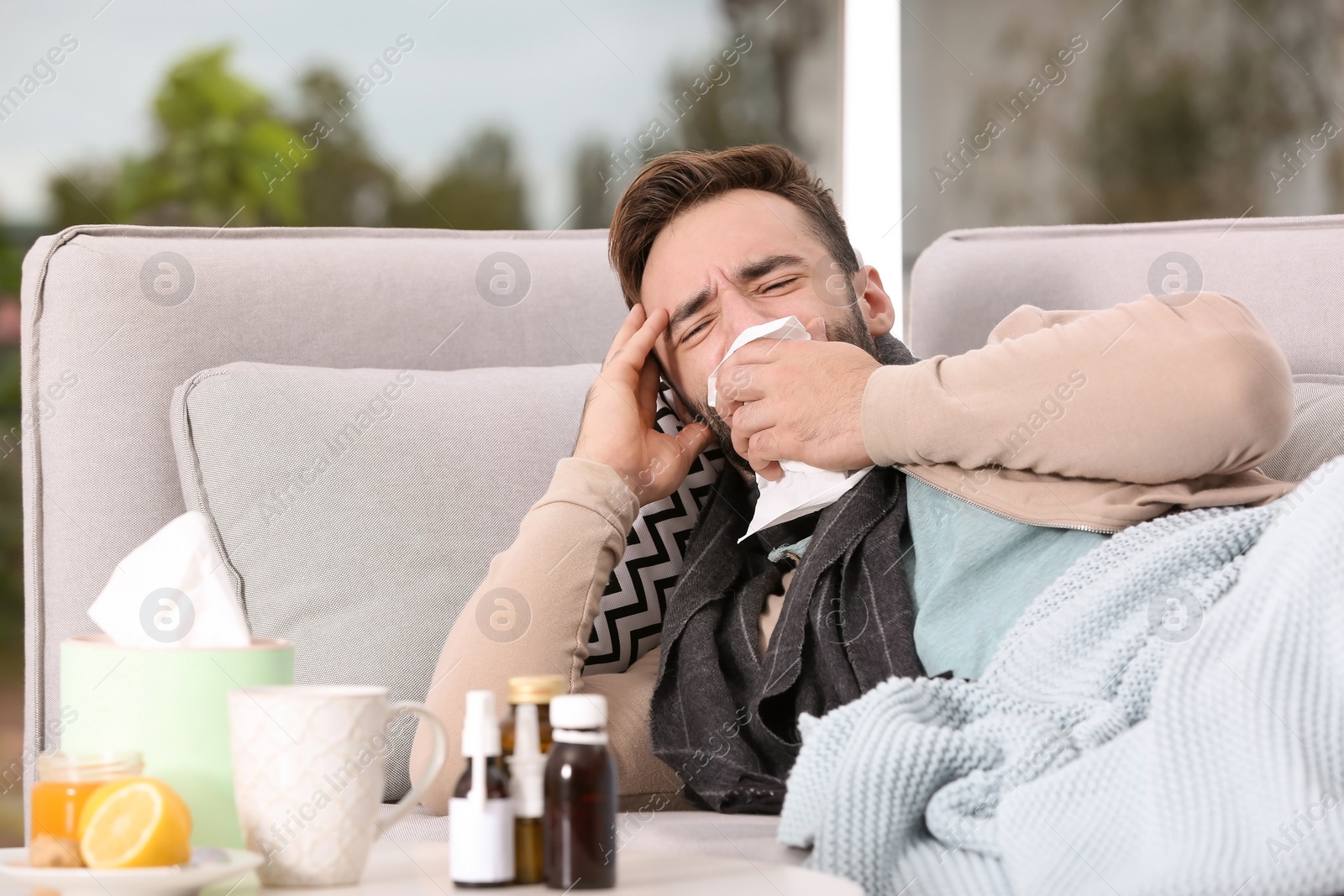 Photo of Ill man suffering from cough on sofa at home