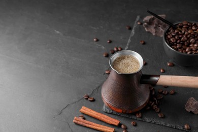 Photo of Cezve with Turkish coffee, beans and cinnamon on dark grey table. Space for text