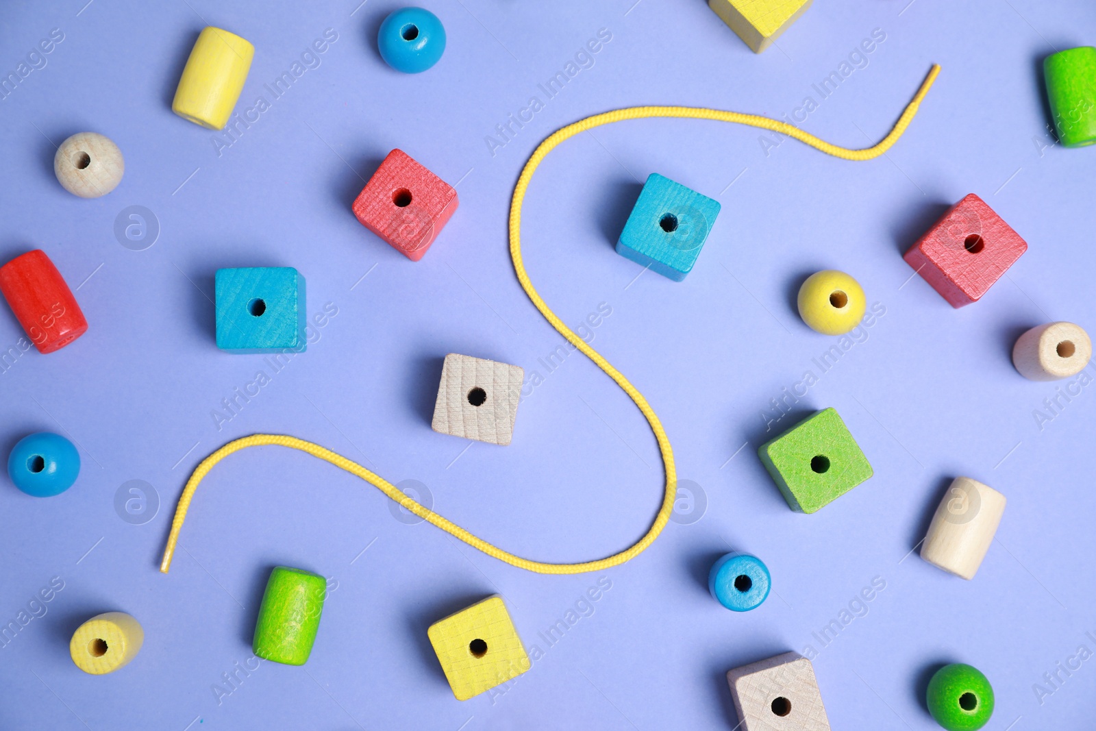 Photo of Wooden pieces and string for threading activity on violet background, flat lay. Educational toy for motor skills development