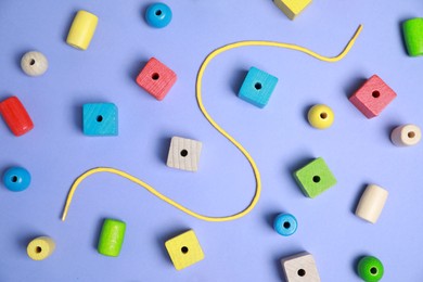 Wooden pieces and string for threading activity on violet background, flat lay. Educational toy for motor skills development