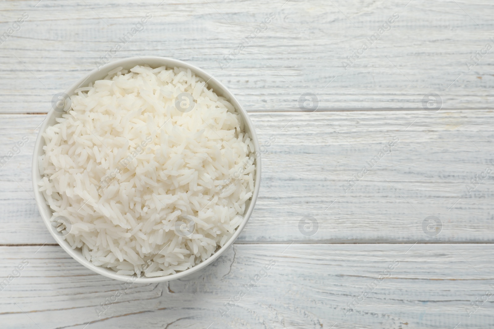 Photo of Bowl of tasty cooked rice on white wooden background, top view. Space for text