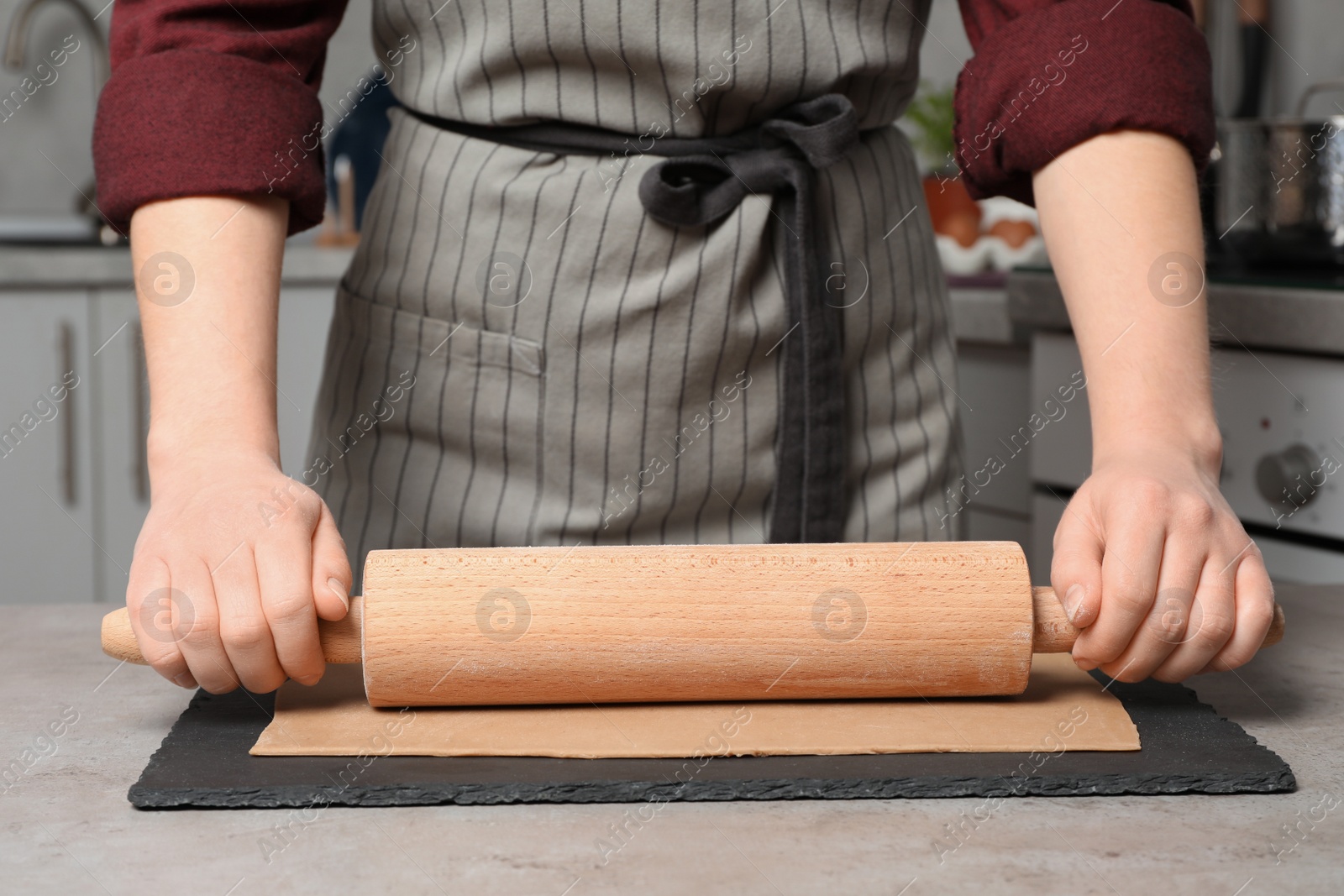 Photo of Woman rolling dough with wooden pin at table in kitchen, closeup