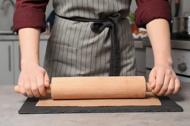 Woman rolling dough with wooden pin at table in kitchen, closeup