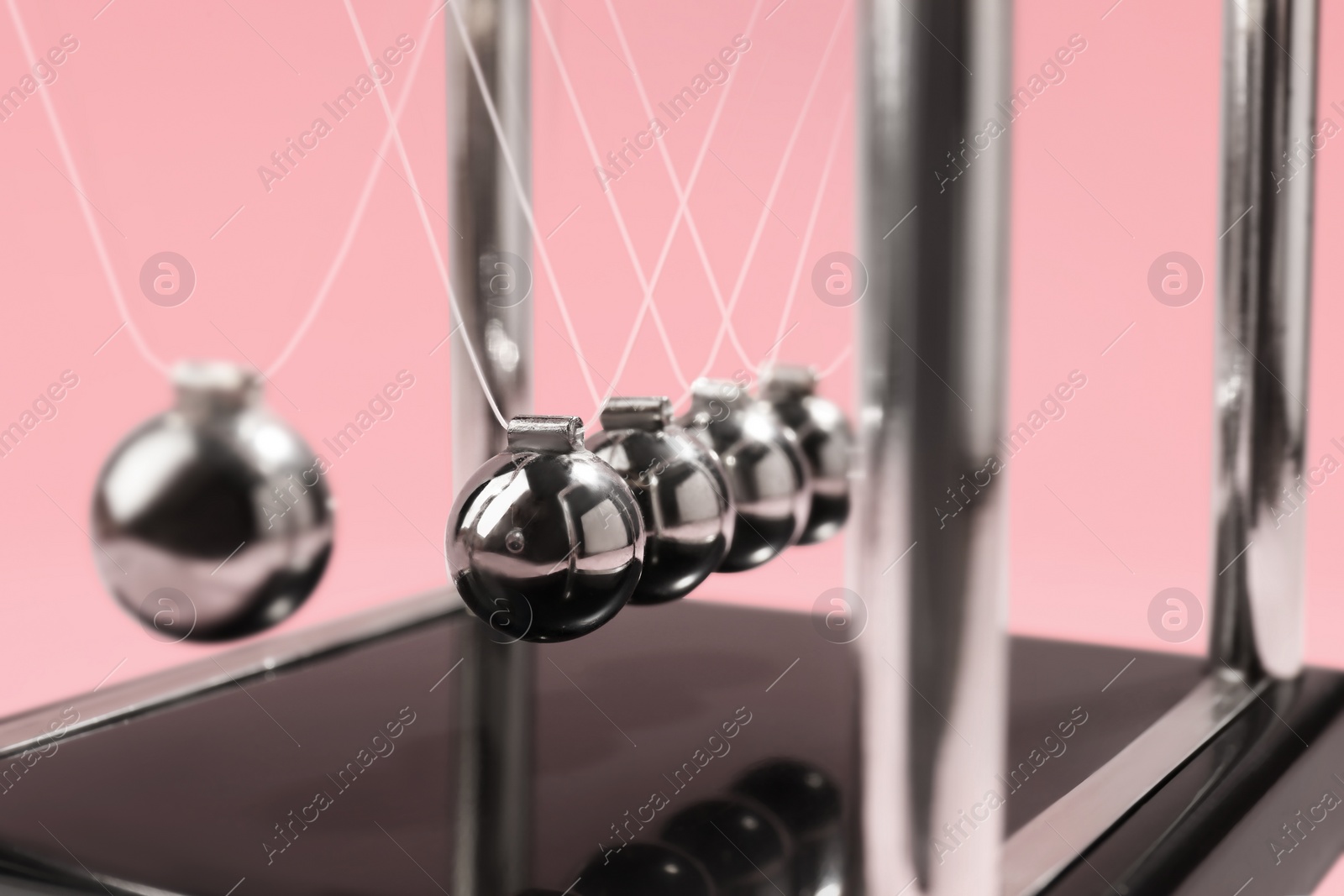 Photo of Newton's cradle on pink background, closeup. Physics law of energy conservation