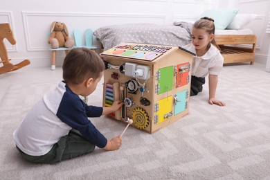 Little boy and girl playing with busy board house on floor in room