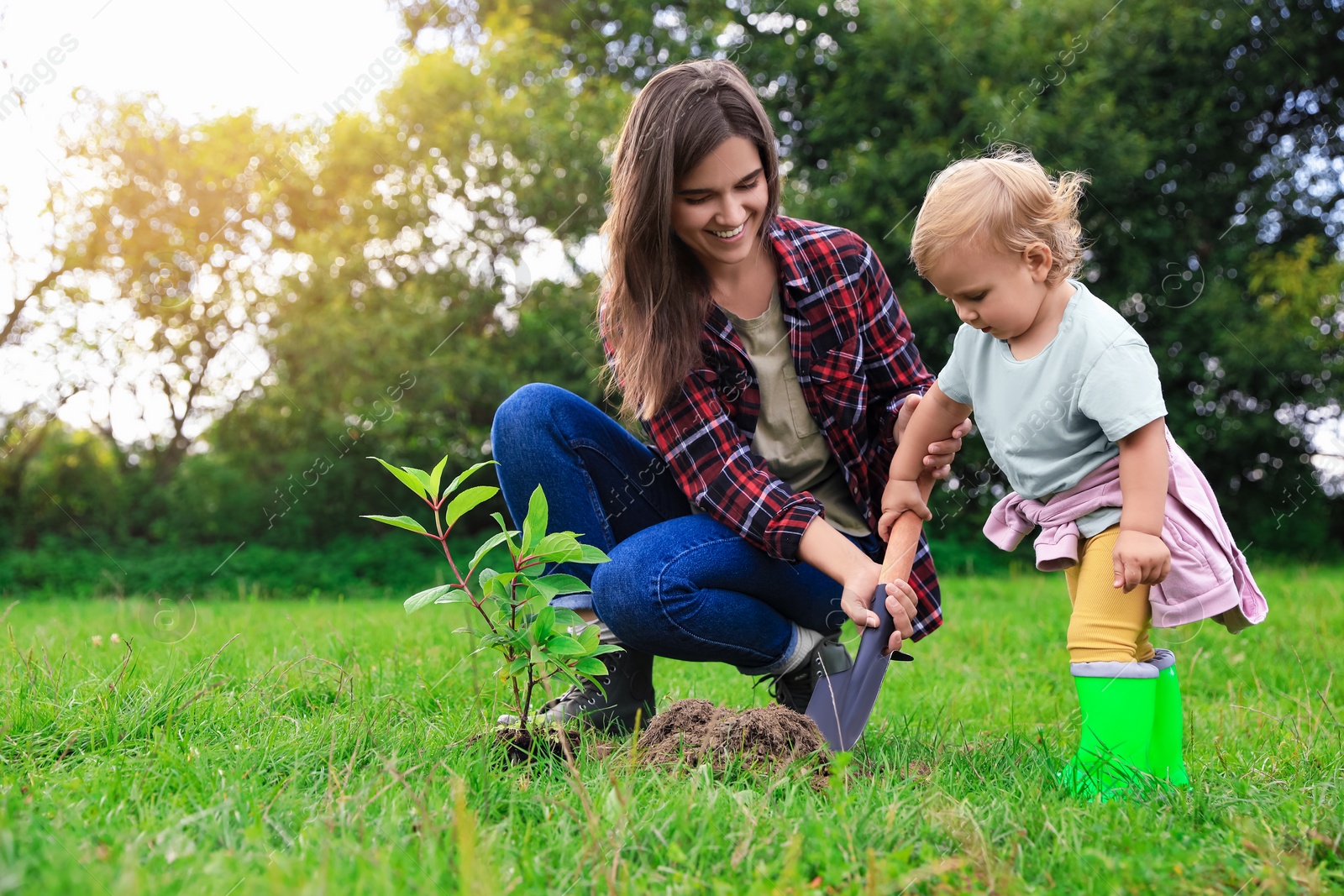 Photo of Mother and her baby daughter planting tree together in garden