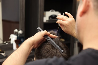 Photo of Professional hairdresser cutting man's hair in barbershop, closeup