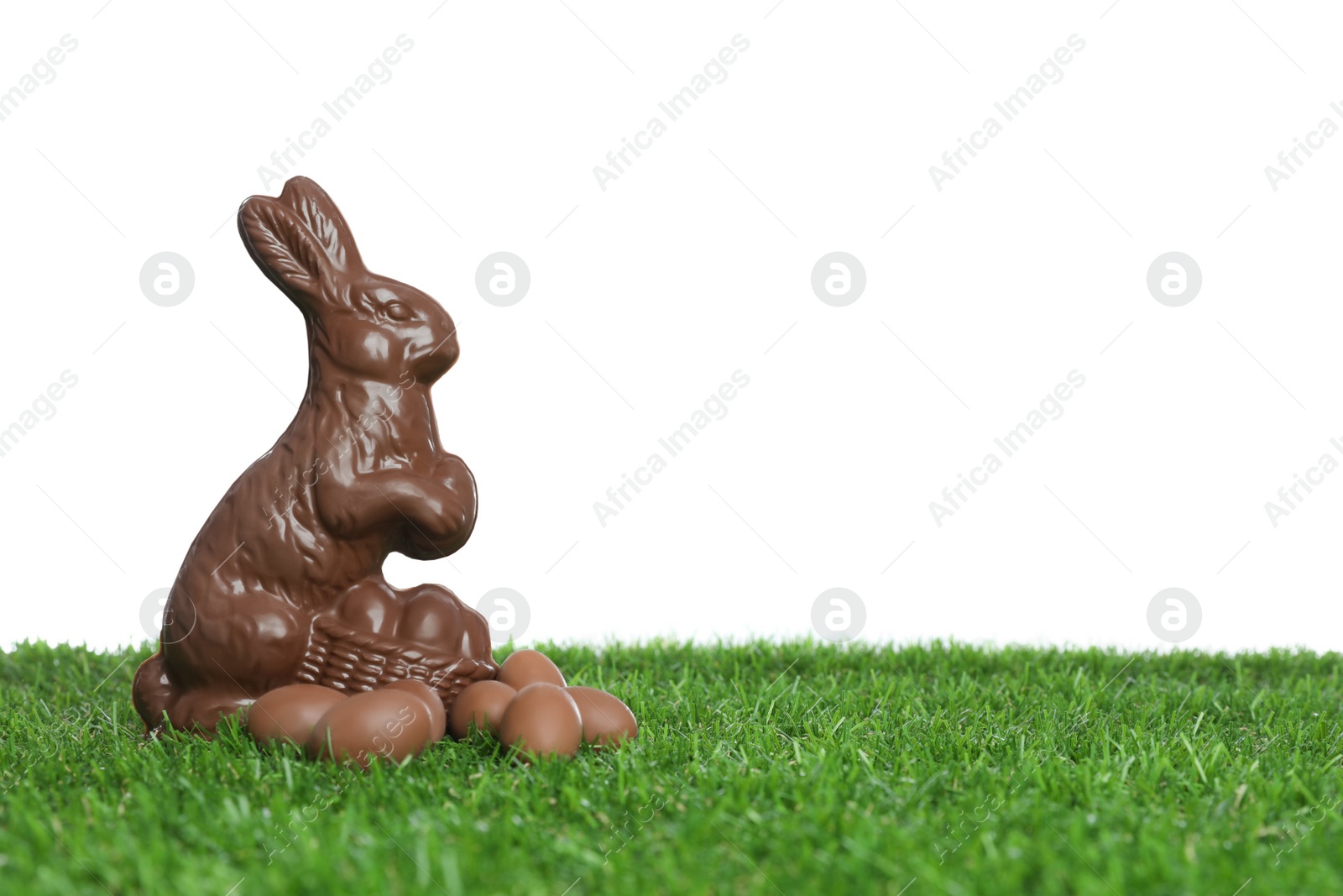 Photo of Chocolate bunny and eggs on green grass against white background, space for text. Easter celebration