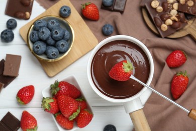 Photo of Dipping fresh strawberry in fondue pot with melted chocolate on white wooden table, top view