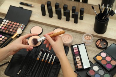 Photo of Professional makeup artist with powder and brush at wooden table, closeup