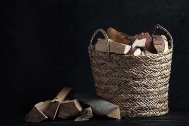 Wicker basket with cut firewood on table against dark background