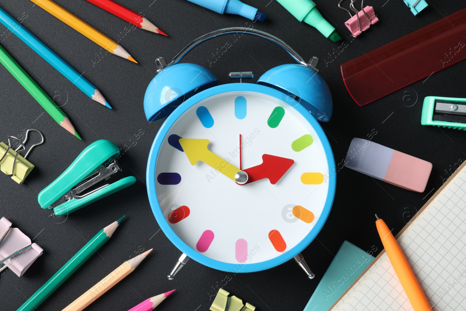 Photo of Flat lay composition with alarm clock and different stationery on black background. School time