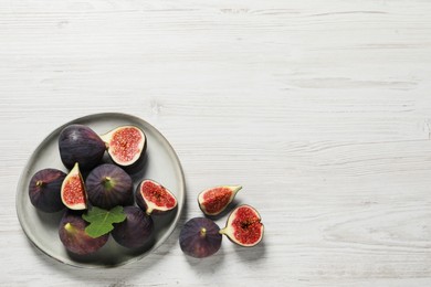 Photo of Whole and cut ripe figs with leaf on white wooden table, flat lay. Space for text