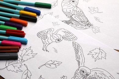 Photo of Drawings for coloring and felt tip pens on table, closeup