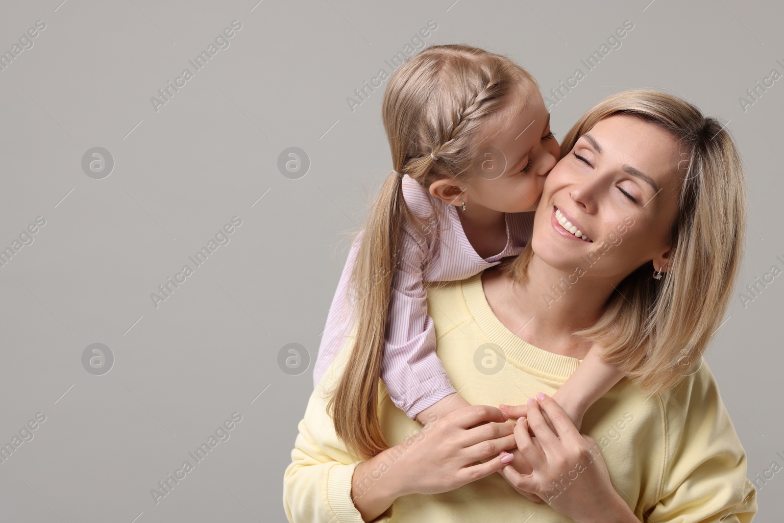 Photo of Daughter kissing her happy mother on grey background. Space for text