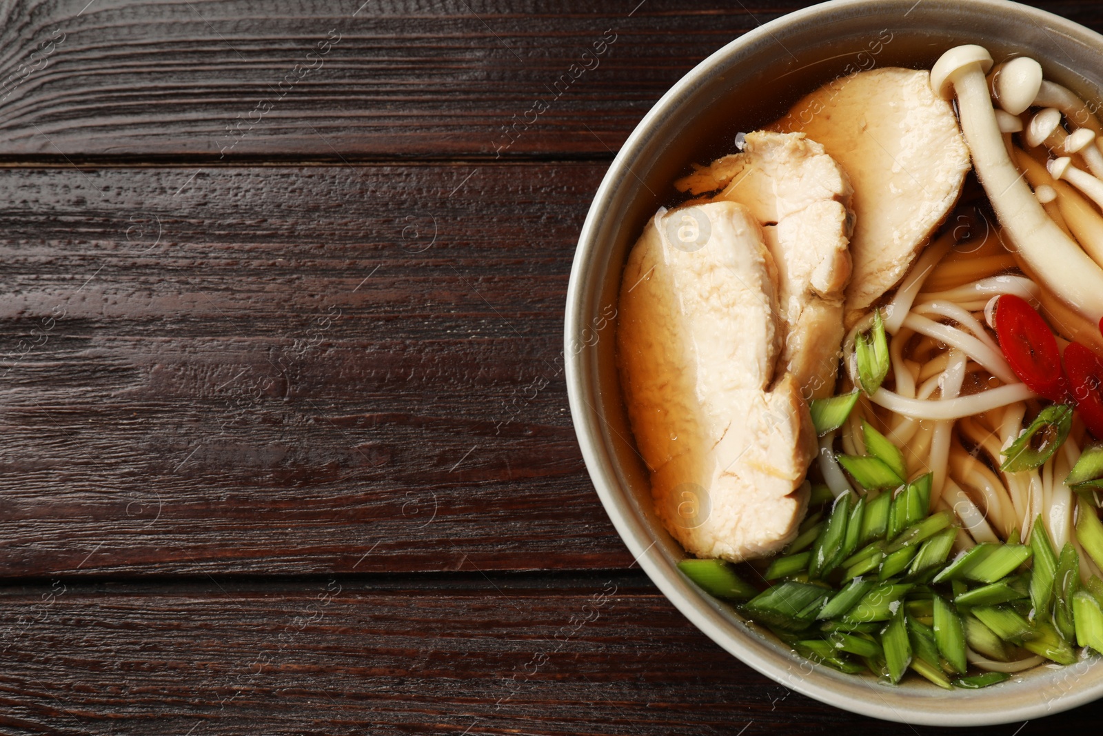 Photo of Delicious ramen with meat and mushrooms in bowl on wooden table, top view. Space for text