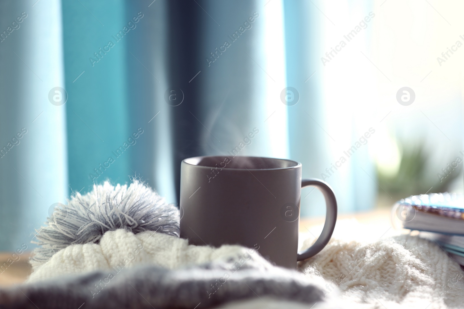 Photo of Delicious morning coffee with knitted hat and scarf near window indoors