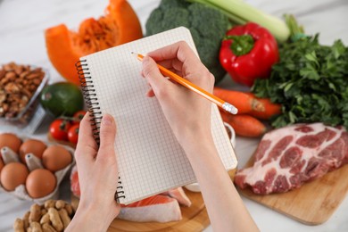 Photo of Woman with notebook and healthy food at white table, closeup. Keto diet