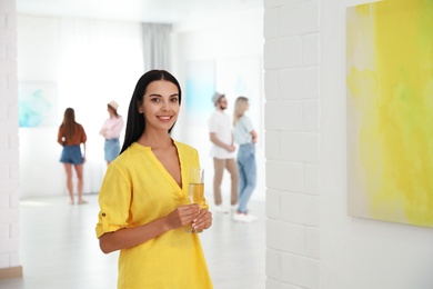 Photo of Young woman with glass of champagne at exhibition in art gallery