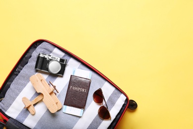 Open suitcase with beach objects on yellow background, top view. Space for text