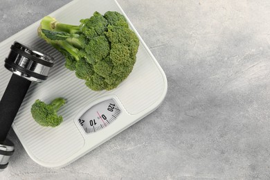 Photo of Healthy diet. Scale, broccoli and dumbbell on grey table, top view. Space for text