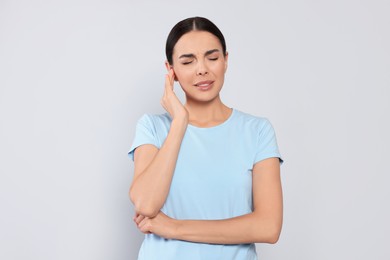 Young woman suffering from ear pain on light grey background