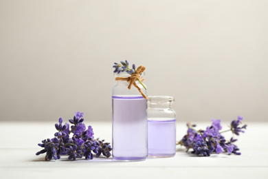 Photo of Bottles of essential oil and lavender flowers on white wooden table