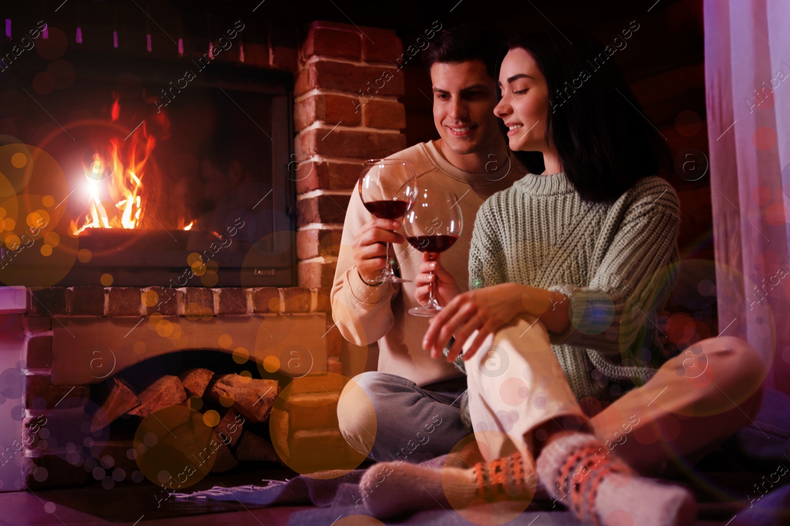 Image of Lovely couple with glasses of wine near fireplace indoors. Winter vacation