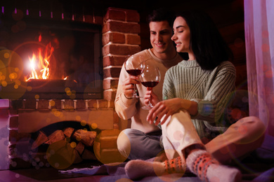 Lovely couple with glasses of wine near fireplace indoors. Winter vacation