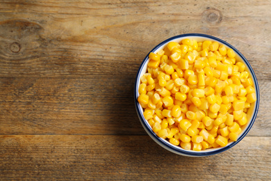 Photo of Delicious canned corn in bowl on wooden table, top view. Space for text