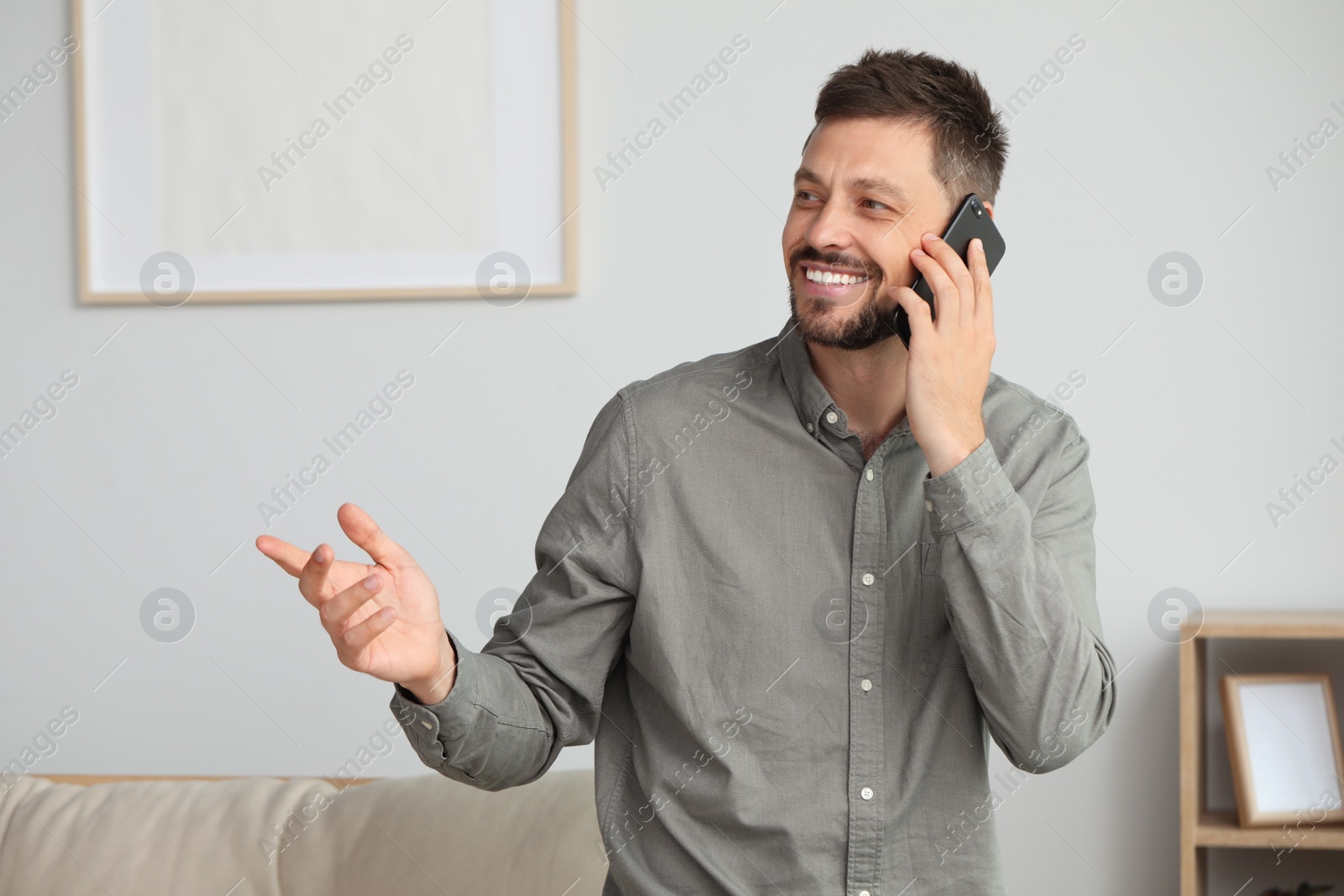 Photo of Happy man talking on smartphone at home