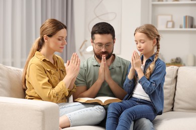 Girl and her godparents praying together on sofa at home