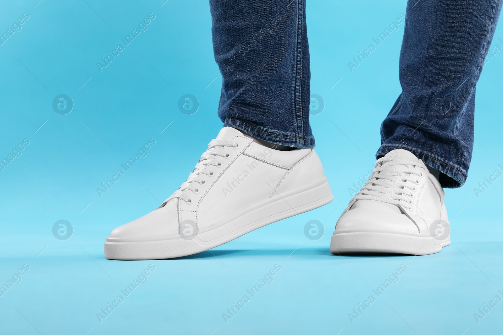 Photo of Man wearing stylish white sneakers on light blue background, closeup