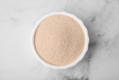 Granulated yeast in bowl on white marble table, top view