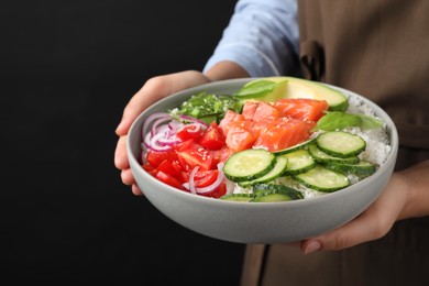 Photo of Woman holding delicious poke bowl with salmon and vegetables on black background, closeup