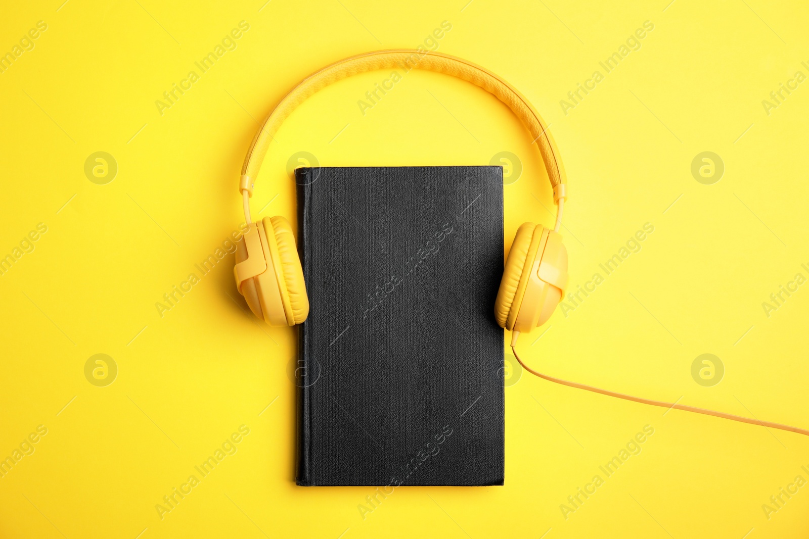 Photo of Book and modern headphones on yellow background, top view