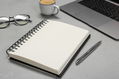 Photo of Open notebook, pen, laptop and glasses on light grey table