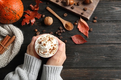 Photo of Woman with cup of tasty pumpkin spice latte at black wooden table, top view