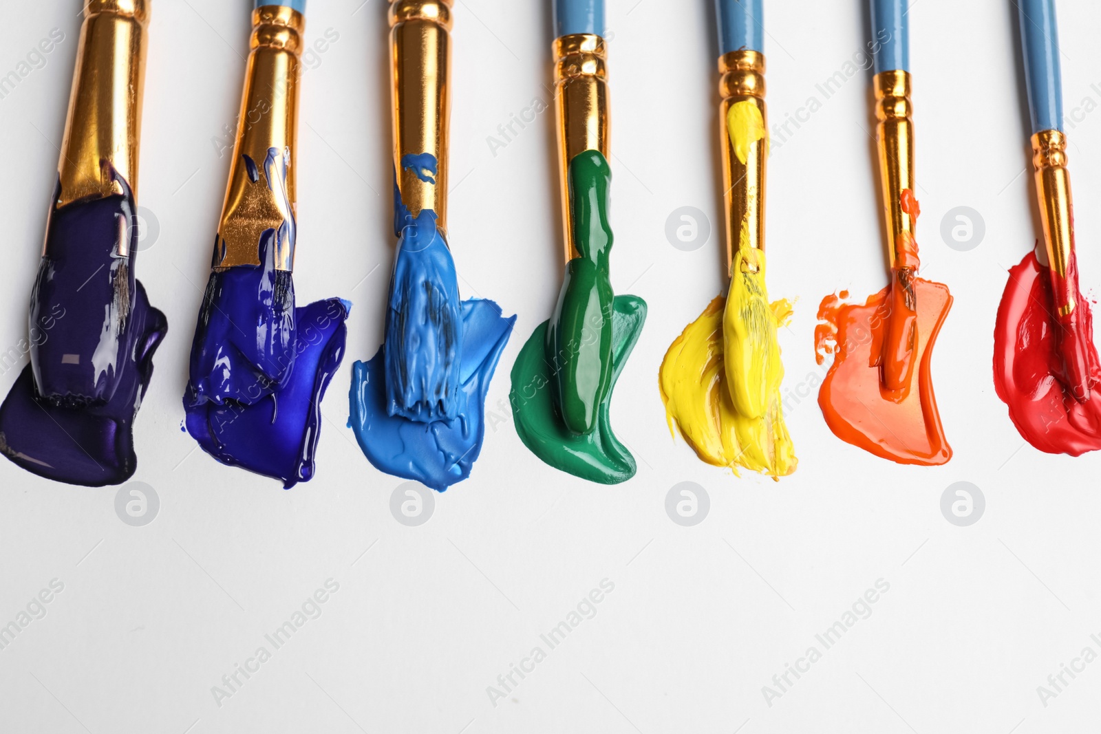 Photo of Set of brushes with different paints on white background, flat lay. Rainbow colors