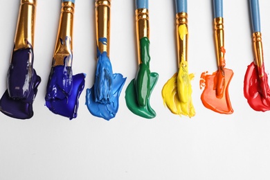 Photo of Set of brushes with different paints on white background, flat lay. Rainbow colors