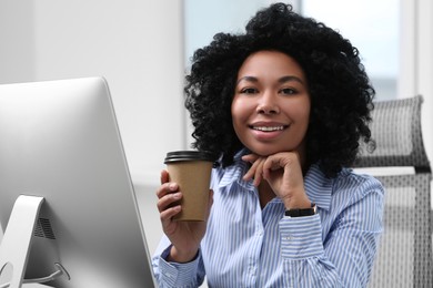 Photo of Young woman with cup of drink working on computer in office