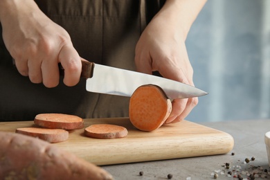 Photo of Woman cutting sweet potato on wooden board, closeup