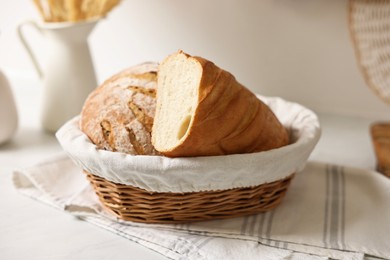 Photo of Wicker bread basket with freshly baked loaf on white marble table in kitchen