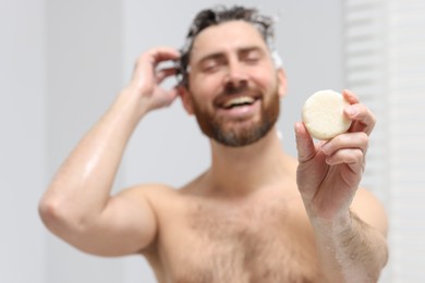 Photo of Happy man showing solid shampoo bar in bathroom, selective focus