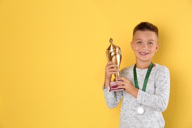 Photo of Happy boy with golden winning cup and medal on yellow background. Space for text