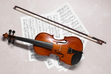 Photo of Violin, bow and music sheets on grey marble table, top view