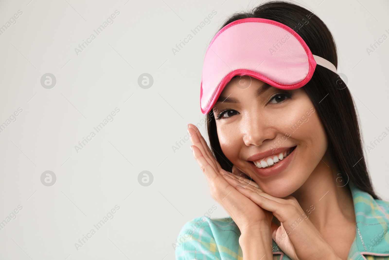 Photo of Beautiful Asian woman wearing pajamas and sleeping mask on light grey background, space for text. Bedtime