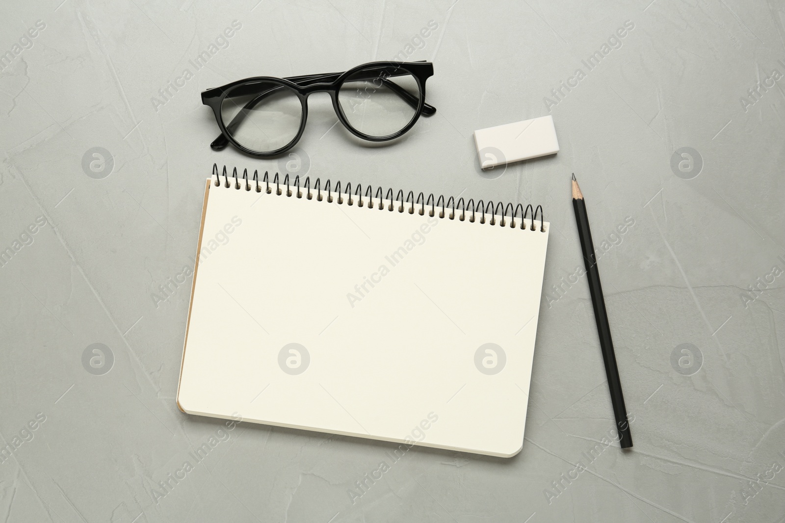 Photo of Sketchbook, glasses, pencil and eraser on light grey table, flat lay