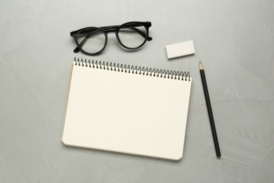 Photo of Sketchbook, glasses, pencil and eraser on light grey table, flat lay