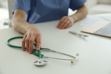 Doctor with stethoscope at white table in hospital, closeup